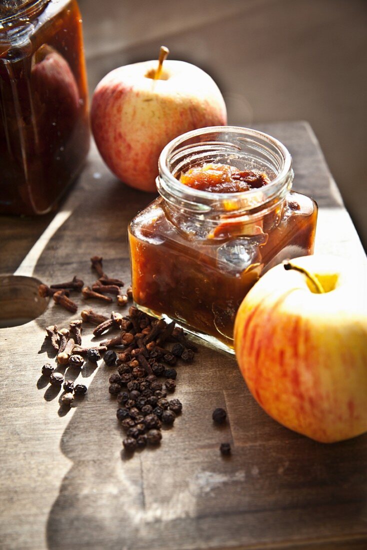 Mehrere Gläser hausgemachtes Apfelchutney, frische Äpfel und Gewürze