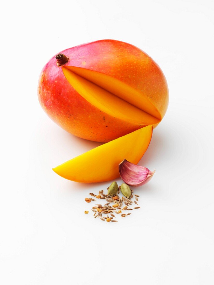 Angeschnittene Mango mit Knoblauchzehe und Gewürzen