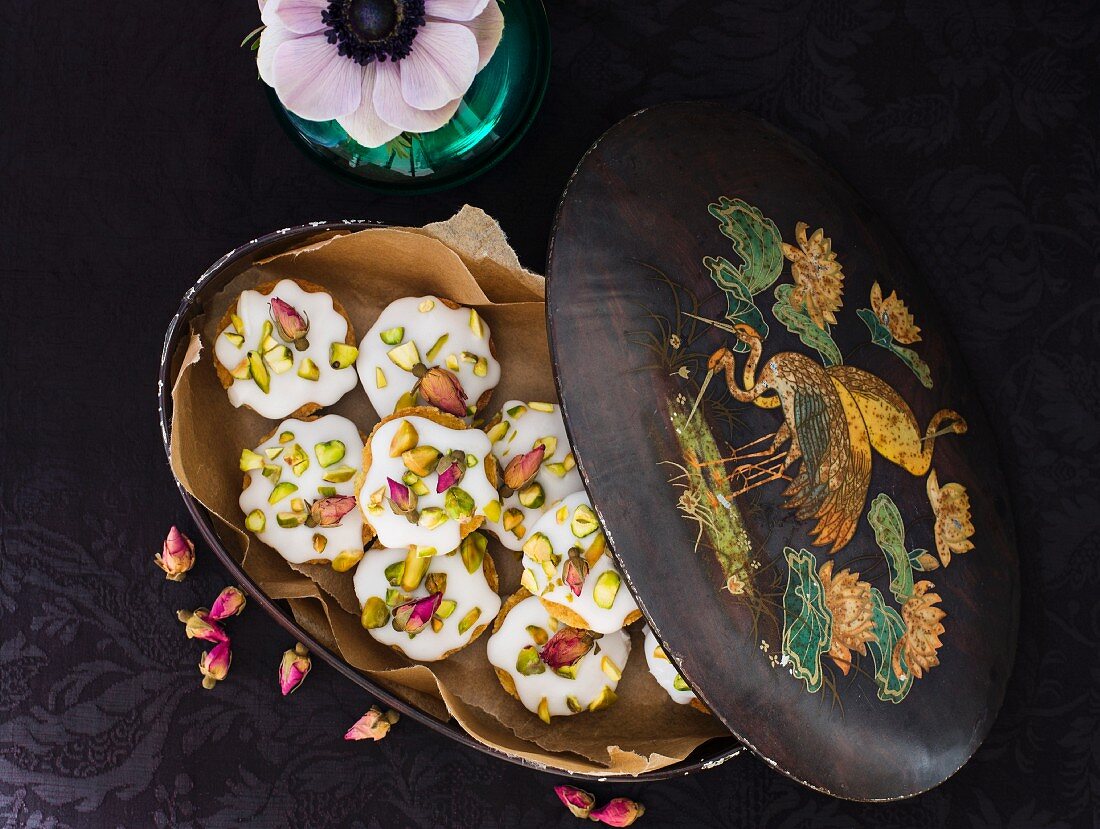 Pistachio cakes topped with icing and rose buds in an old tin