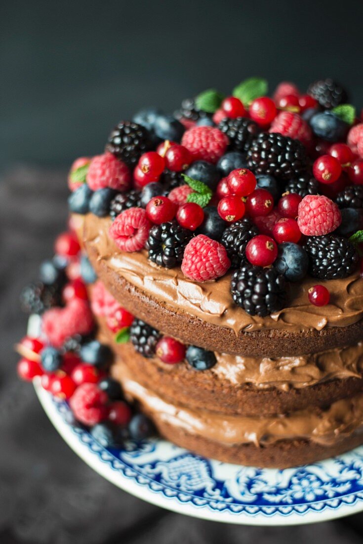 A layered chocolate cream cake decorated with berries and mint leaves