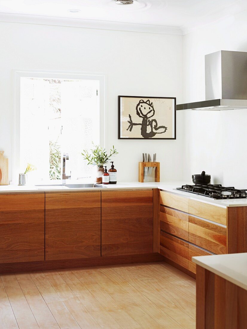 Modern L-shaped kitchen counter with solid wooden base units and framed child's drawing on wall next to window