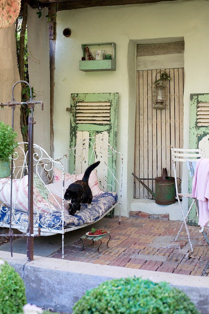 Katze auf Vintage Metallbett auf Veranda eines Bauernhauses