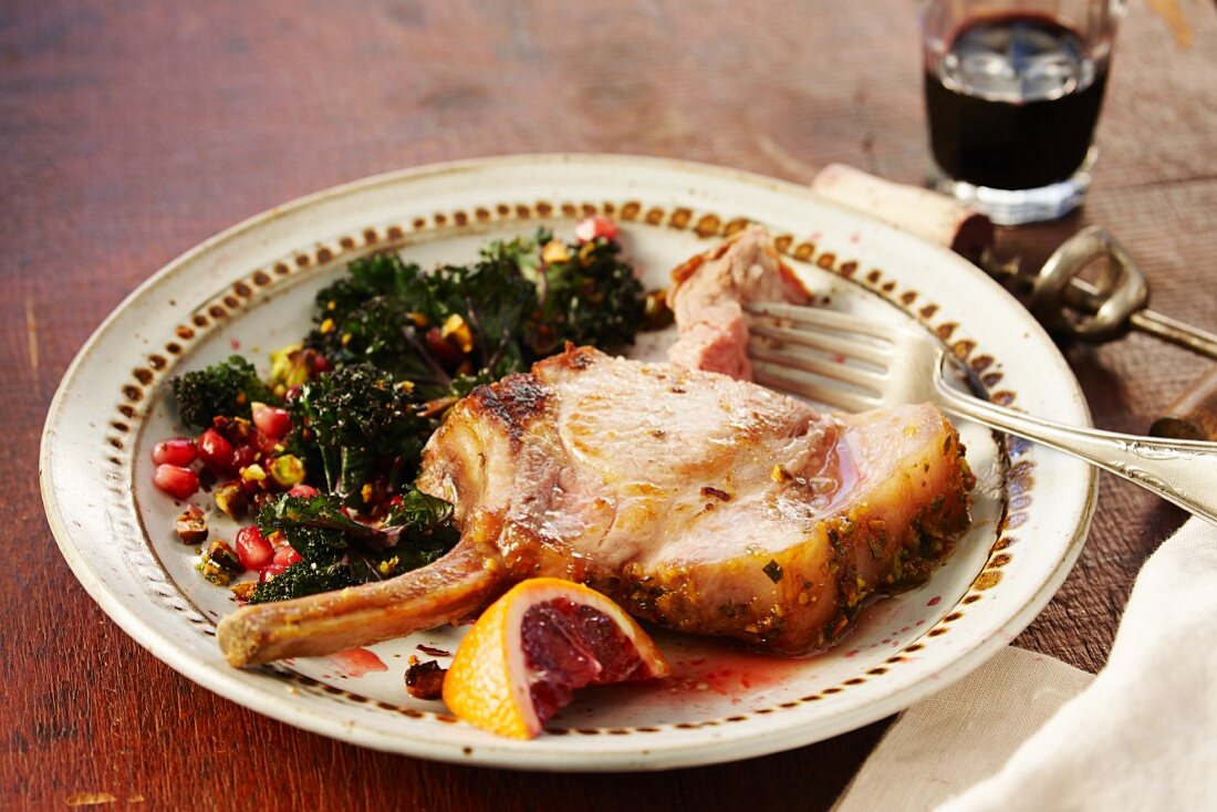 A pork chop with pomegranate seeds, green kale and blood oranges