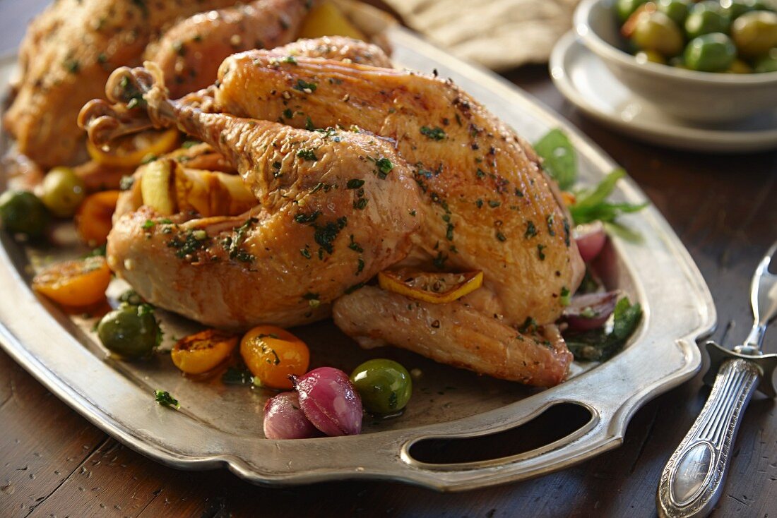 Two roast chickens with lemon, olives, onions and herbs
