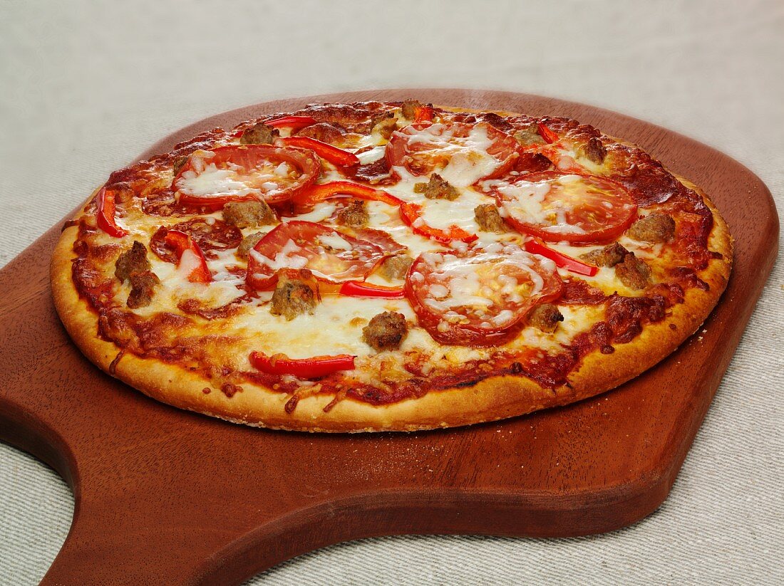 A pizza topped with pepperoni, pepper and mozzarella on a chopping board