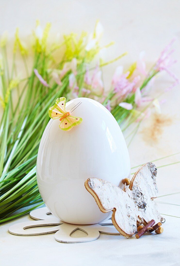 A white egg decorated with butterflies in front of spring flowers