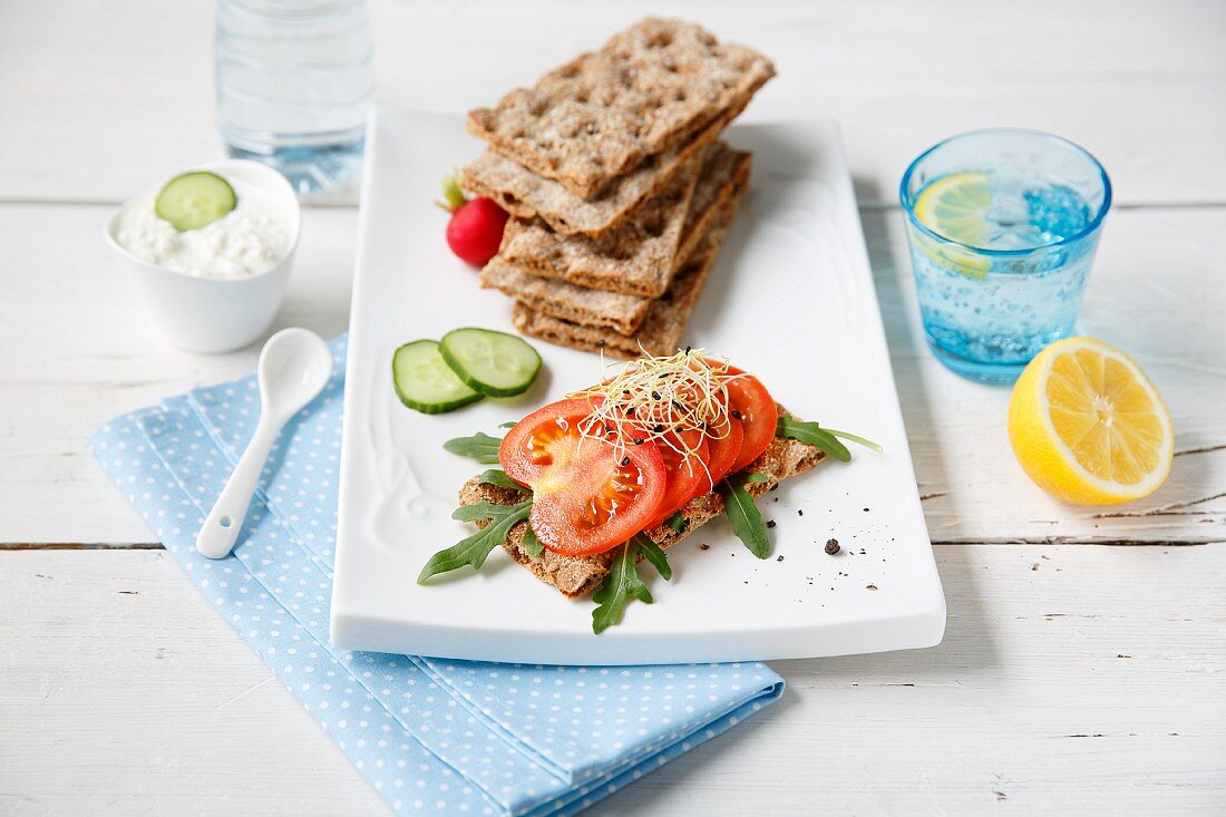 Crisp bread with a dip, tomatoes, cucumber, rocket and lemon water