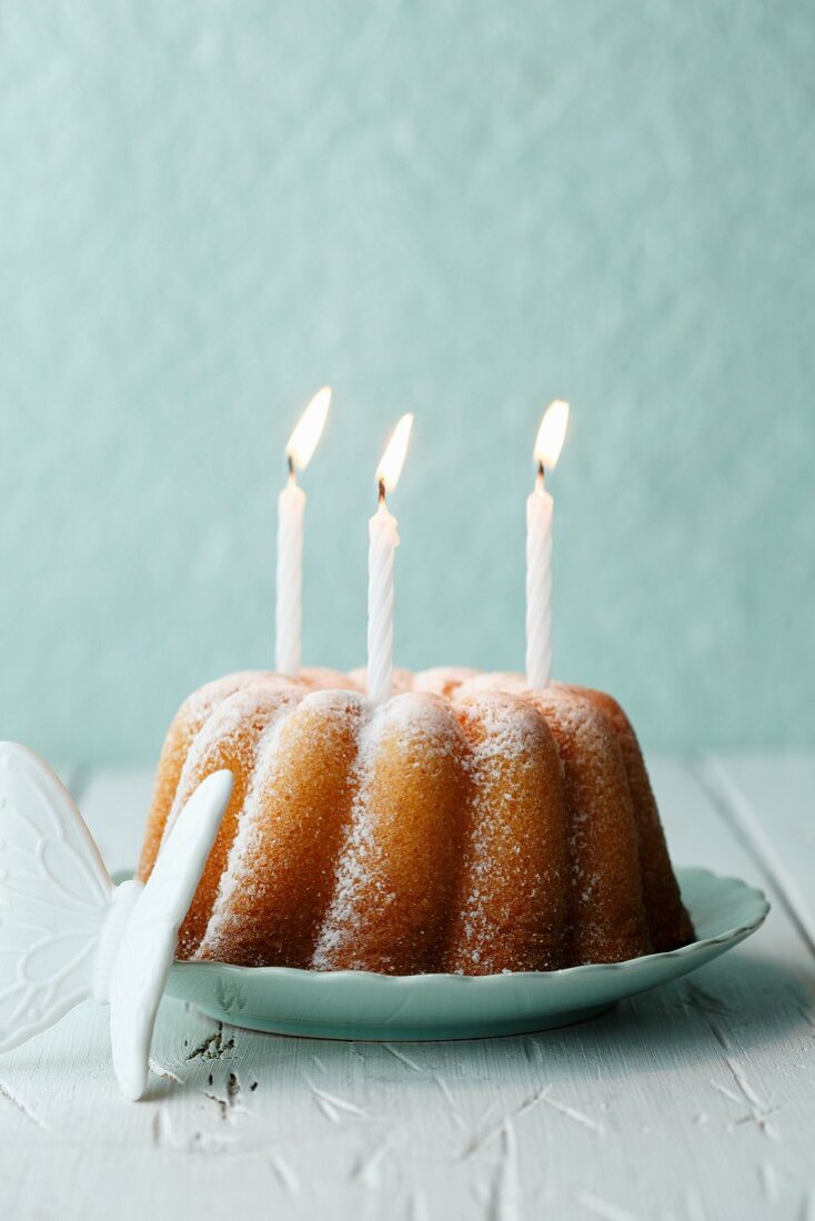Lemon cake with icing sugar and three burning candles
