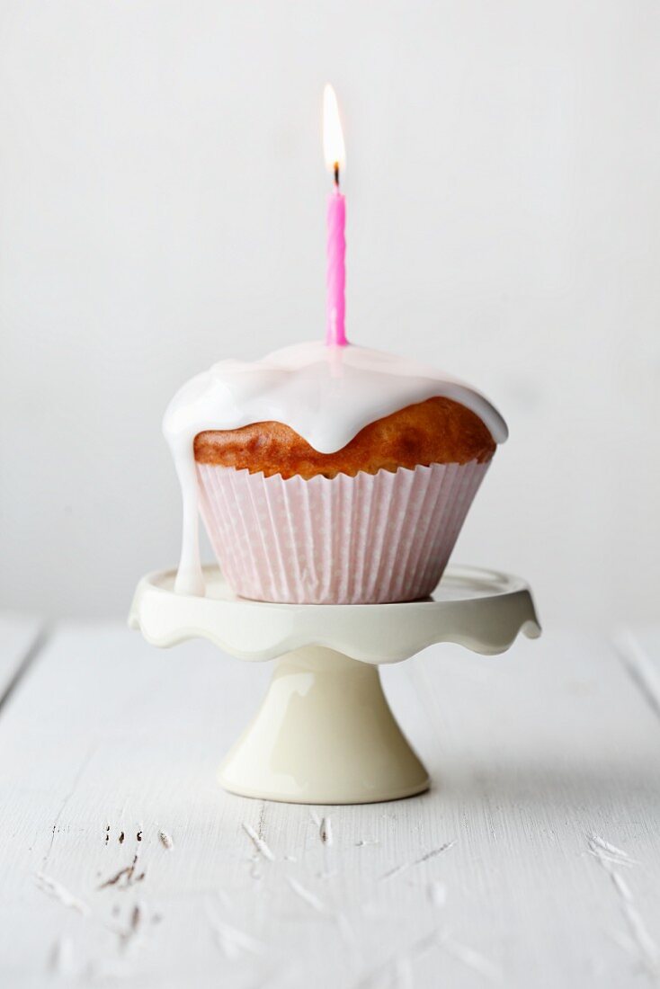 A muffin with dripping icing and a burning candle