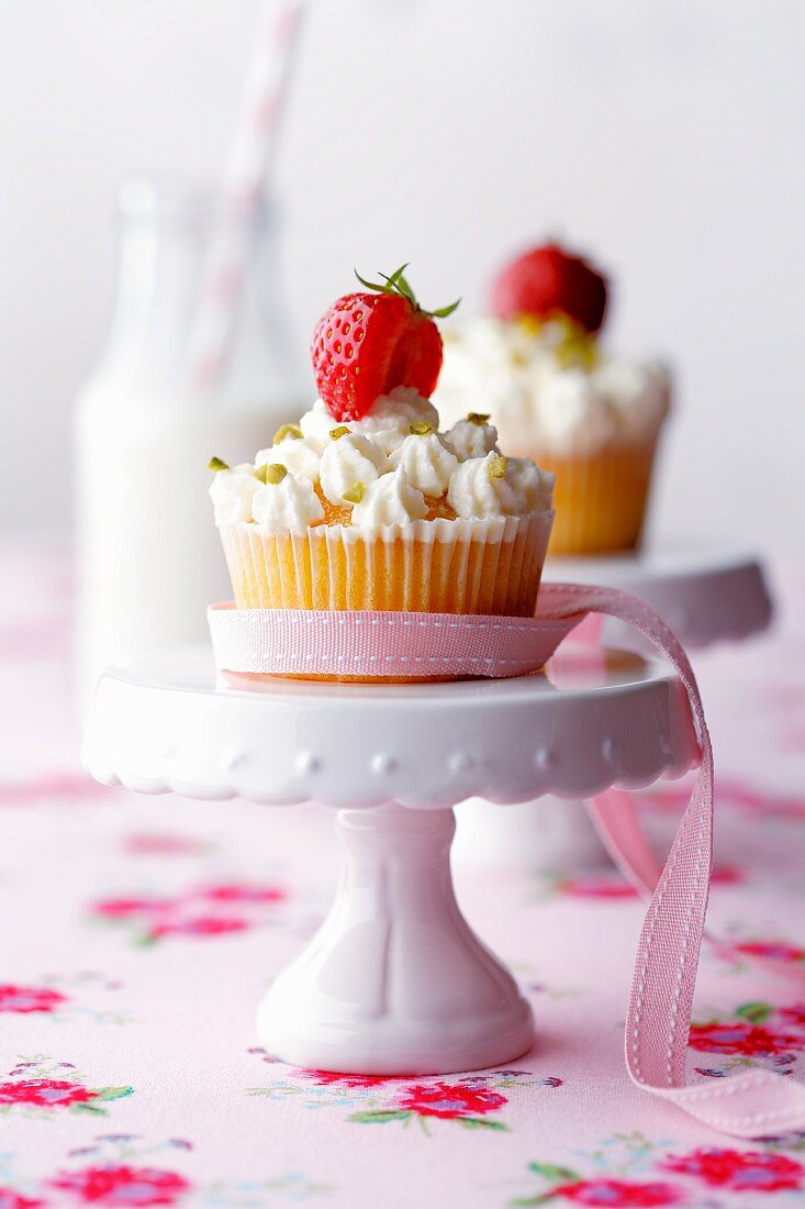 Erdbeer-Joghurt-Cupcakes auf Etageren mit rosa Schleife, Milchflasche mit Strohhalm im Hintergrund