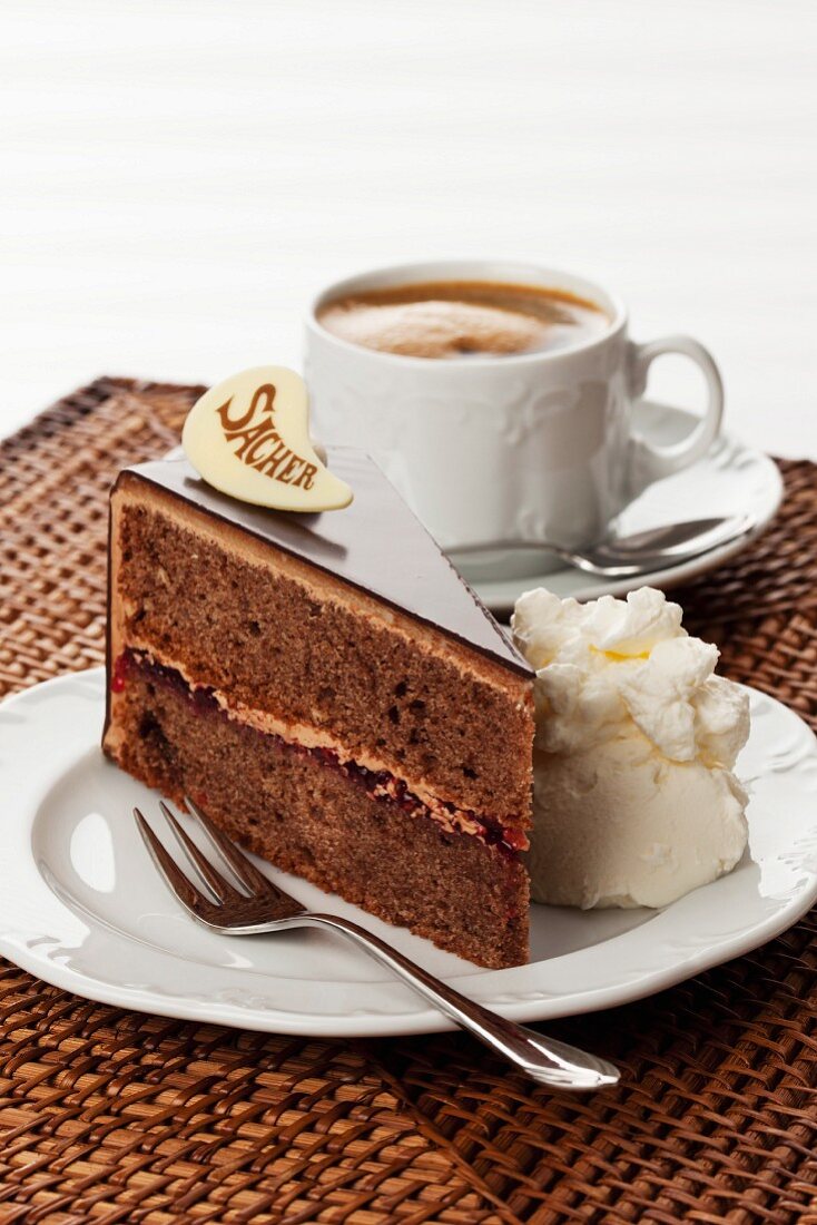 A slice of Sachertorte (rich Austrian chocolate cake) with cream served with a cup of coffee