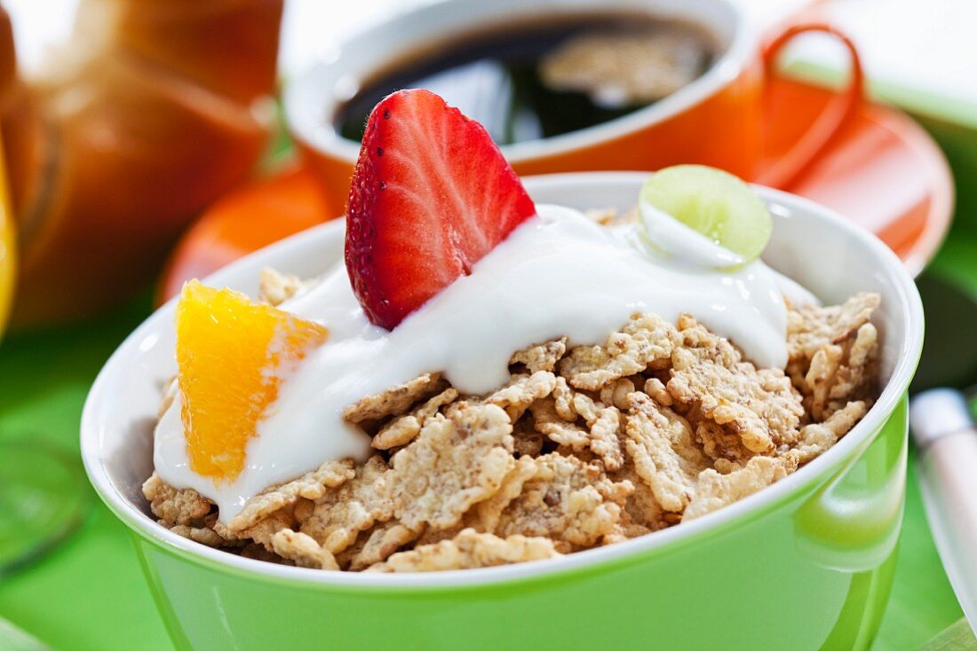 A bowl of muesli with yogurt and fruit served with a cup of coffee and a croissant