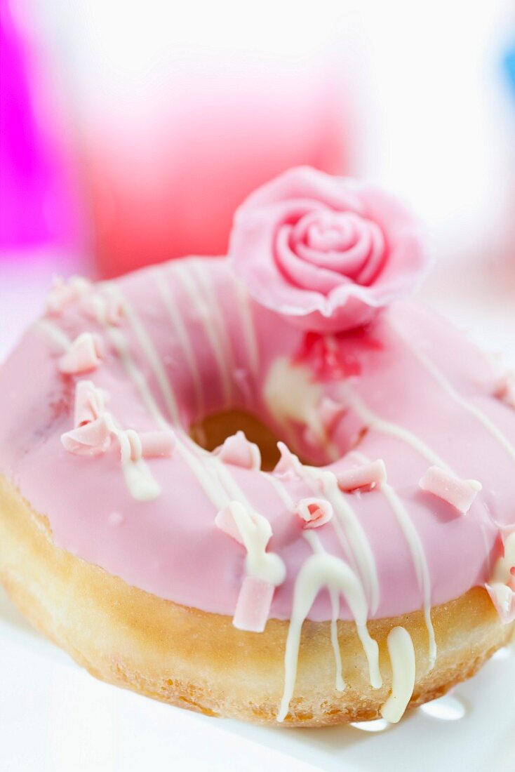 A doughnut topped with pink icing and a sugar rose