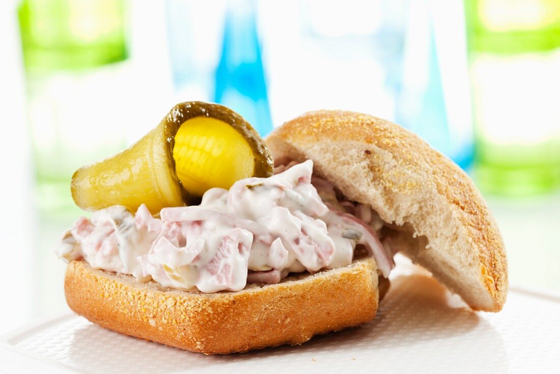 A bread roll filled with a creamy meat salad and gherkins