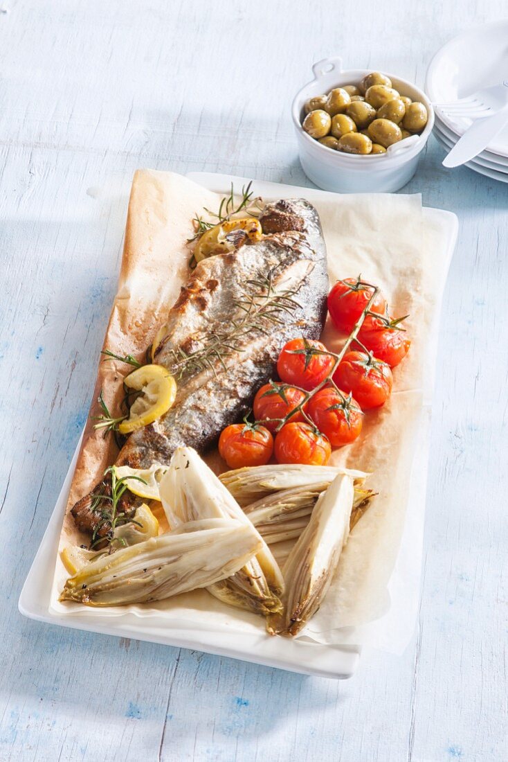 Fried fish with chicory and cherry tomatoes on baking paper