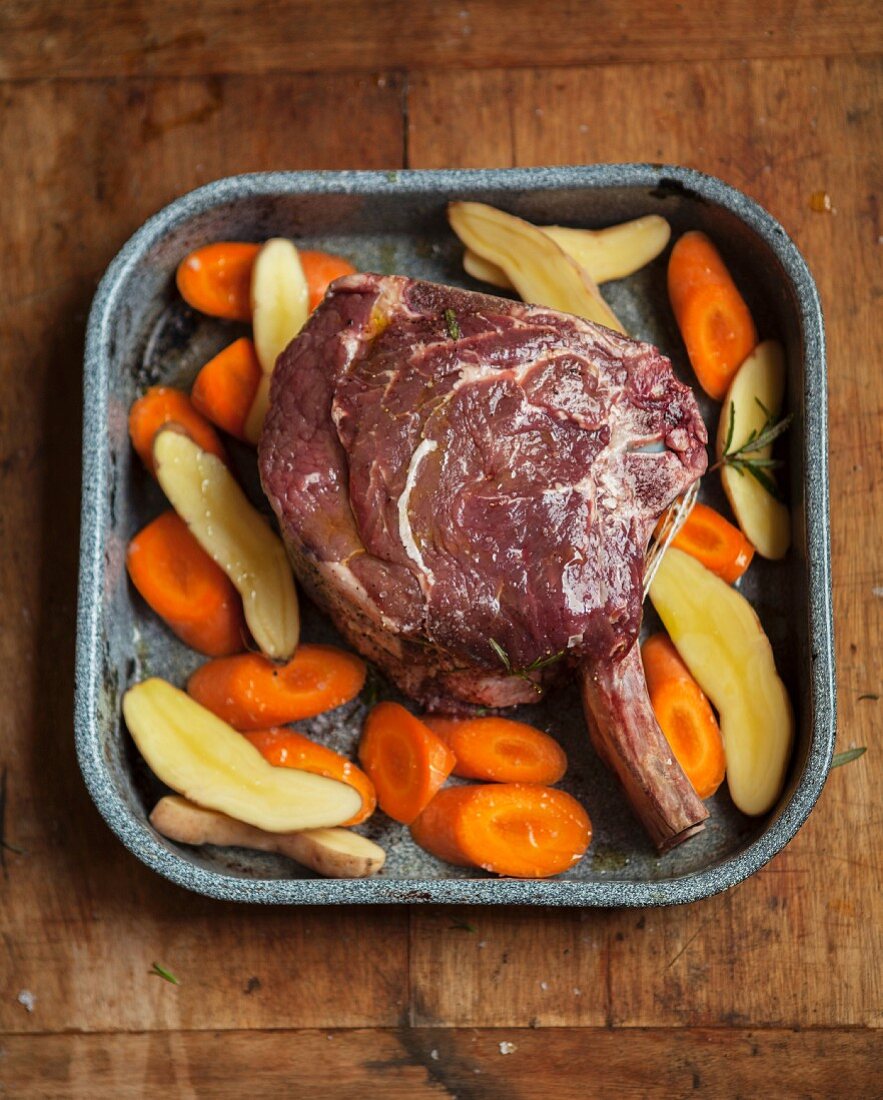 A rack of beef ribs with vegetables on a baking tray ready to roast