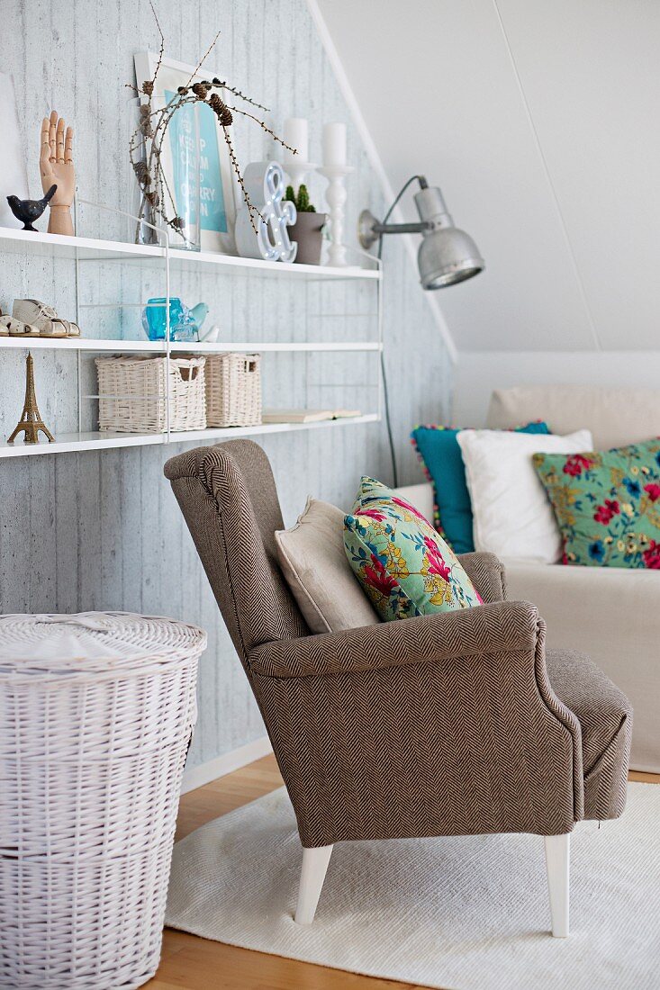 Vintage ornaments on floating shelves above white-painted wicker basket and armchairs with floral scatter cushions