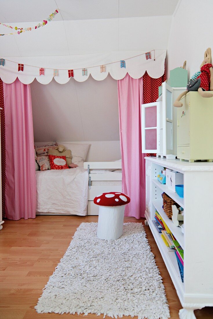 Vorhang und Schabracke mit Girlande vor einer Bettnische im romantischen Mädchenzimmer; davor ein Fliegenpilzhocker