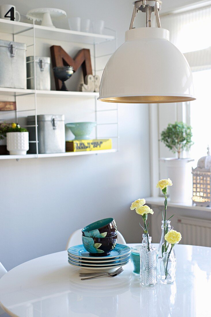 Retro lamp above crockery and yellow carnations in glass vases on white dining table