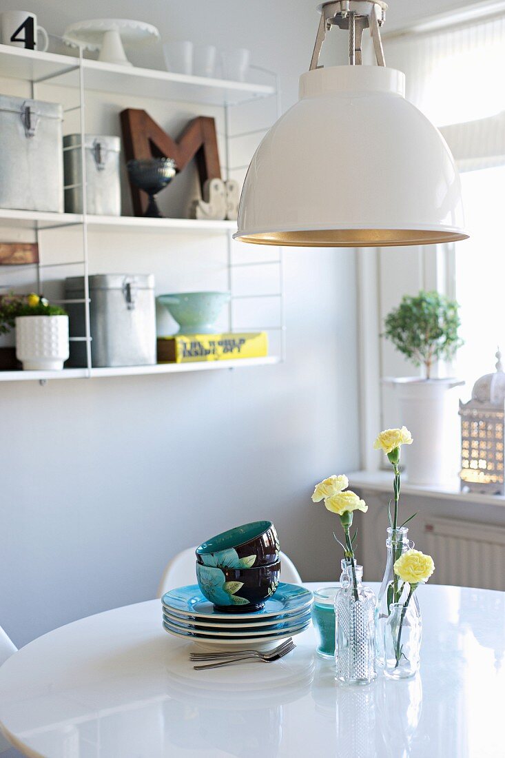 Retroleuchte über weißem Esstisch mit Geschirr und gelben Nelken in Glasvasen