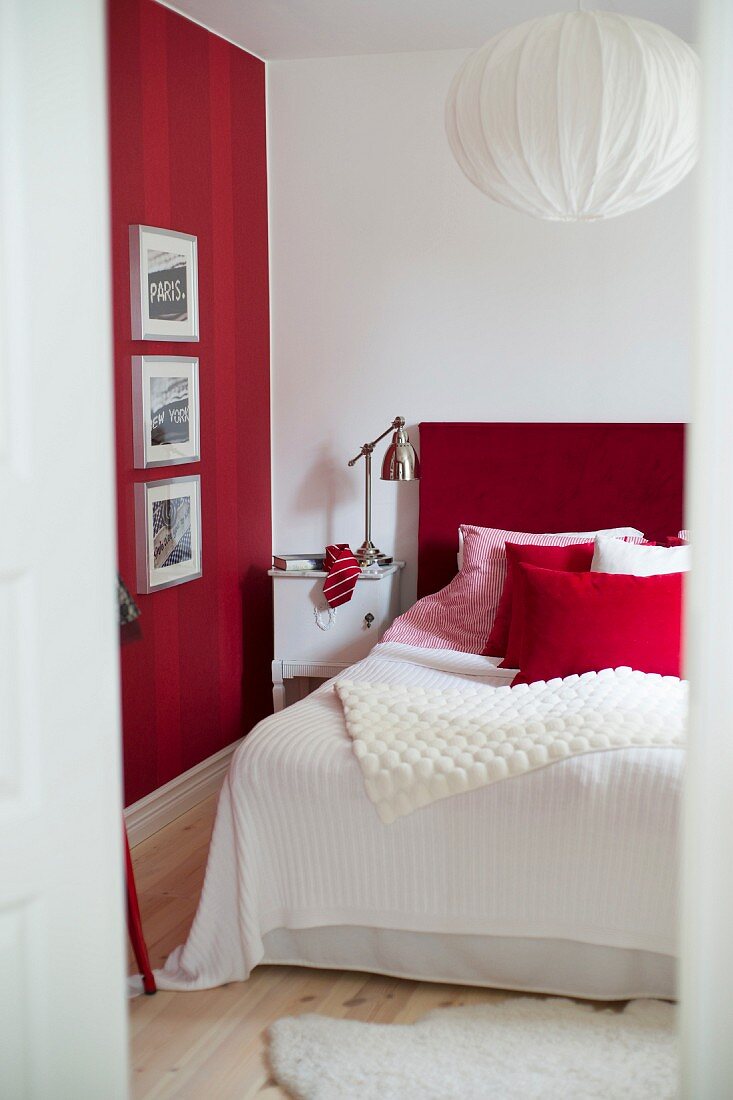 Framed pictures on red striped wall, bed with red headboard and retro-style lamp on bedside table