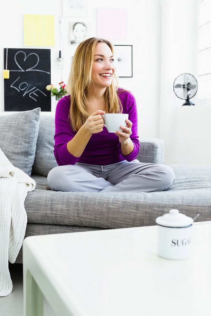 A woman sitting on a sofa holding a cup of tea