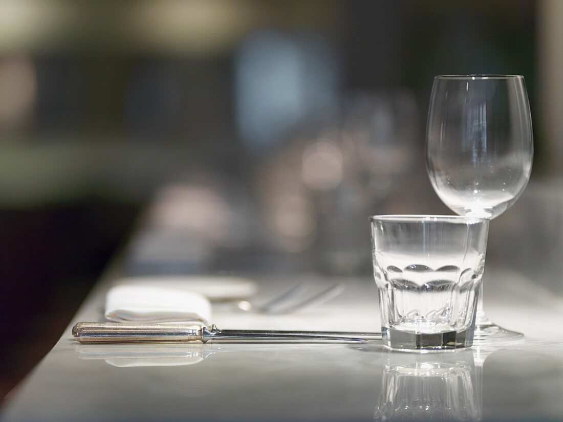 A place setting in a restaurant with glasses, cutlery and a napkin