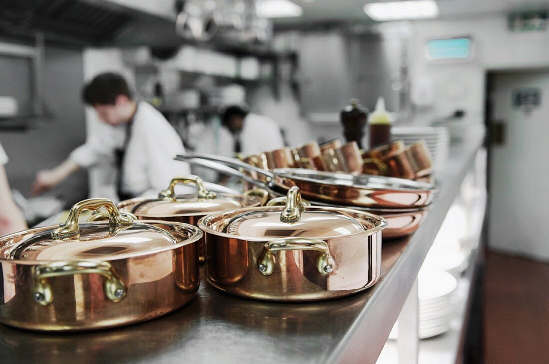 Copper pots in a restaurant kitchen with chefs working in the background