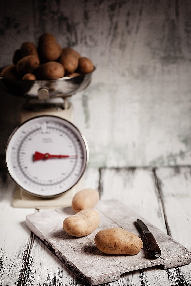 Potatoes on a chopping board and on an old pair of kitchen scales