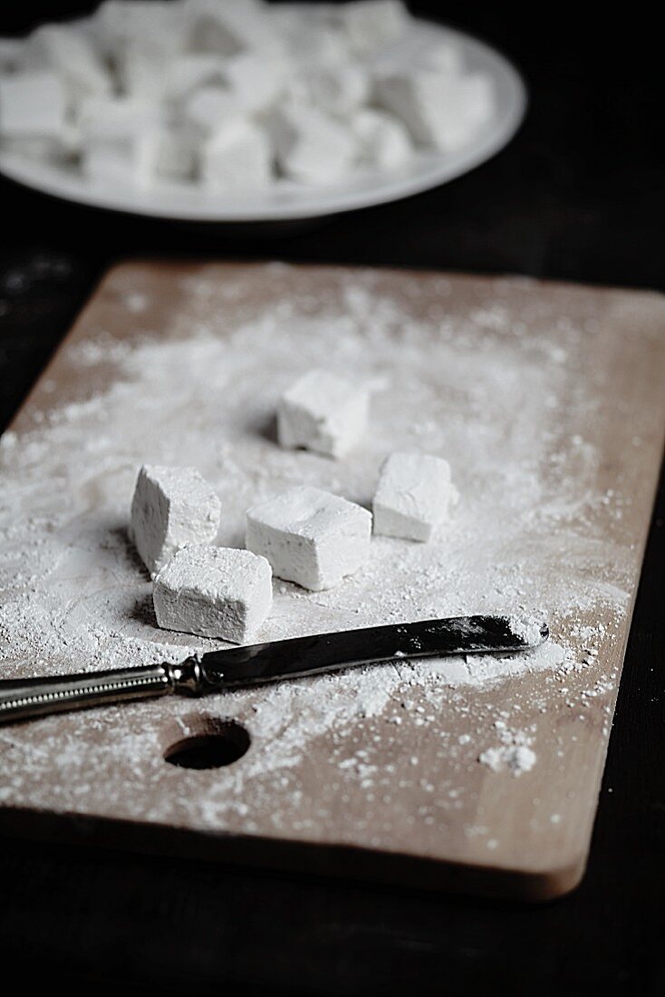 Selbstgemachte Marshmallows mit Puderzucker auf Schneidebrett und in Schüssel