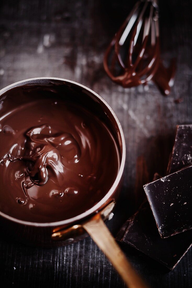 Geschmolzene Schokolade im Kupfertöpfchen, daneben Schokoladenstücke