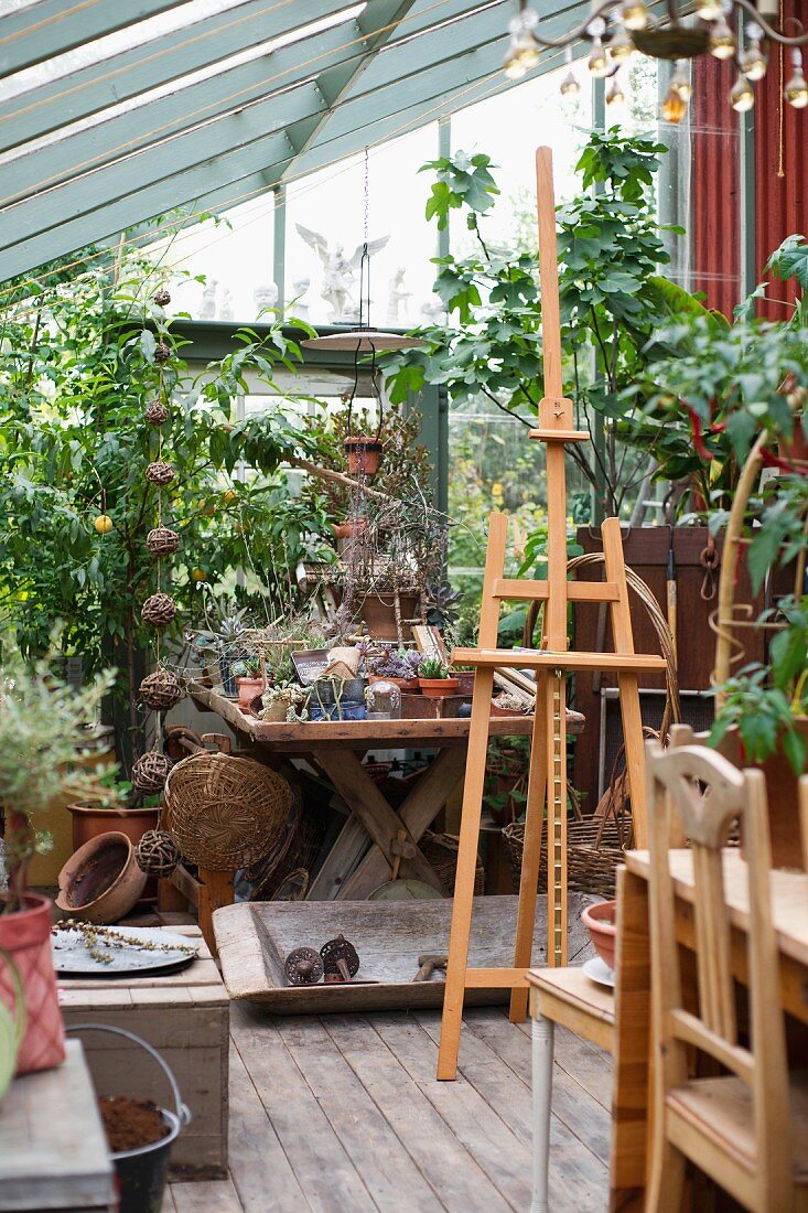 Staffelei vor Pflanzentöpfen und Gartenzubehör in Gewächshaus