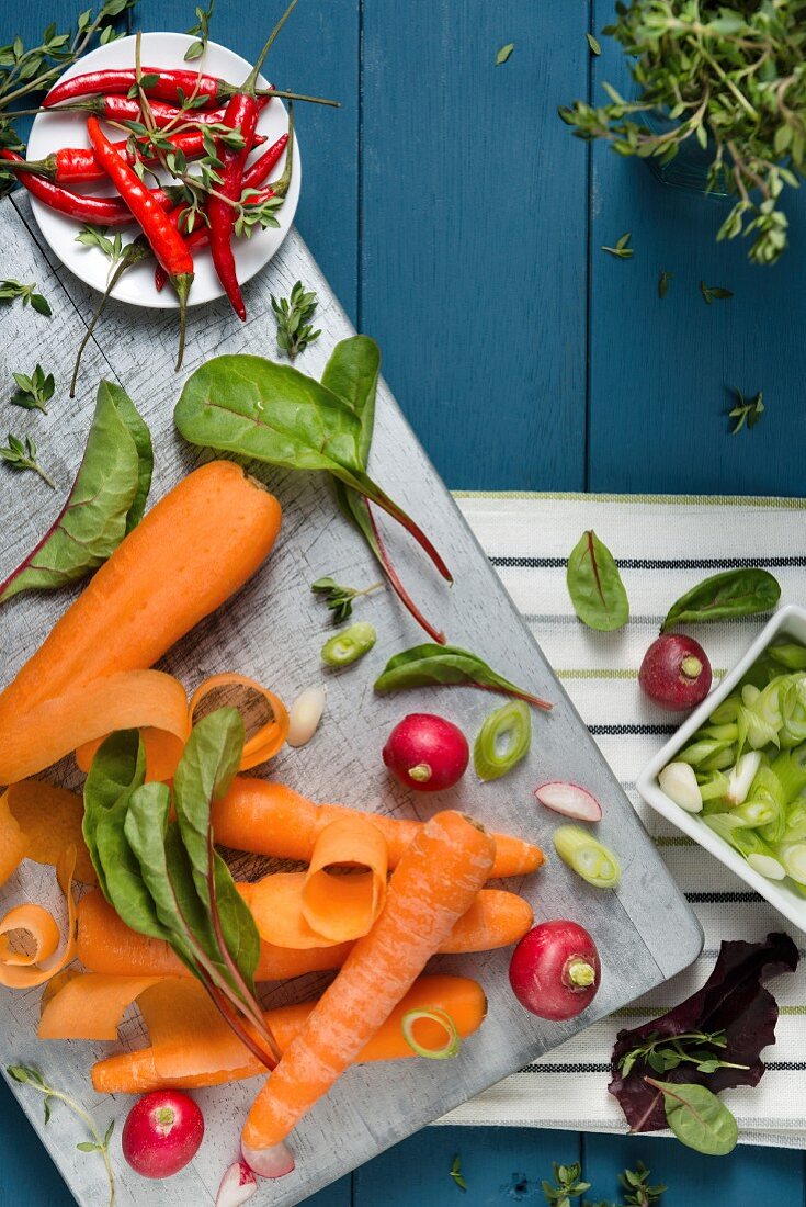 An arrangement of vegetables featuring carrots, radishes and chilli peppers on a chopping board