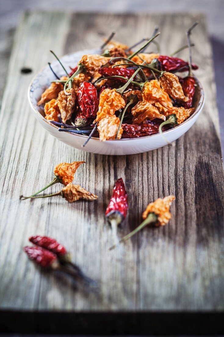 Various different dried chilli peppers on a wooden board and in a bowl