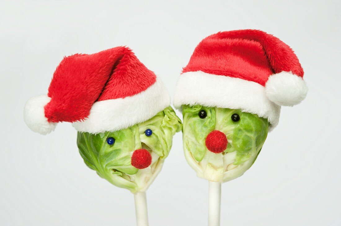 Two Brussels sprouts on sticks with Christmas hats and faces