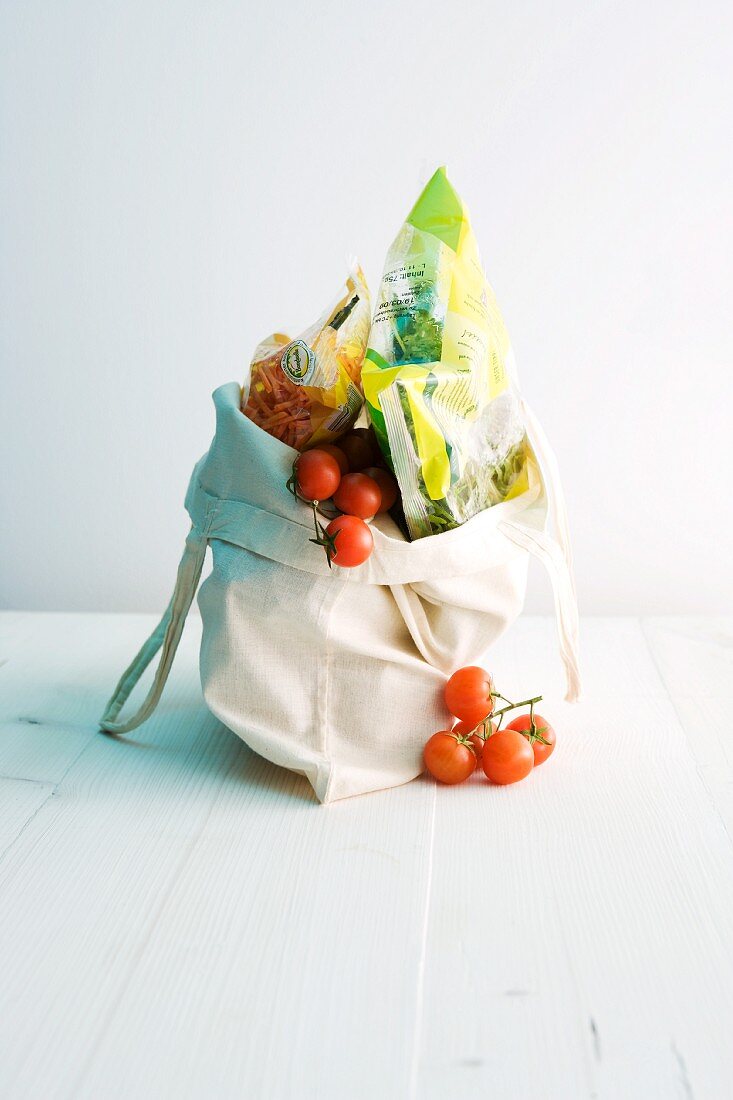 Einkaufstasche mit Kirschtomaten und verpackten Lebensmitteln