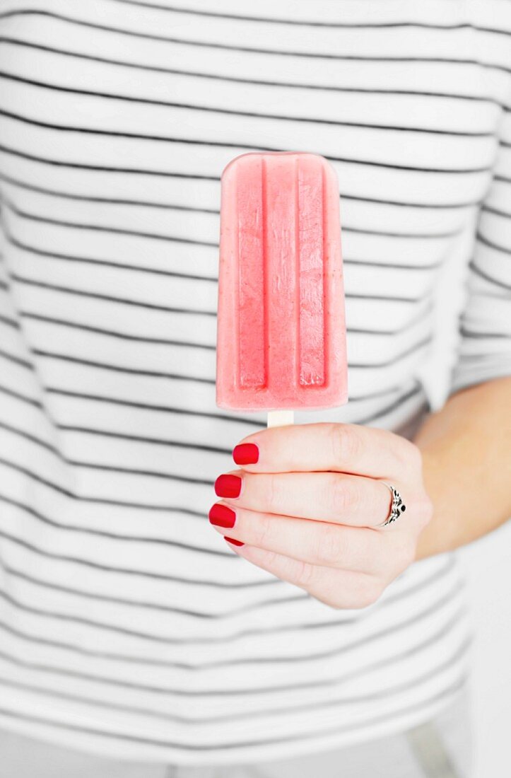 A hand with varnished fingernails holing a pink ice lolly