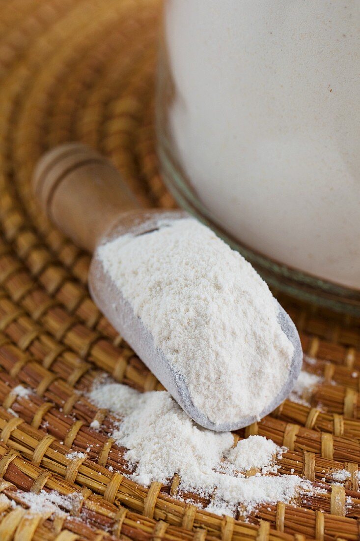 Cassava flour in a scoop next to a storage jar