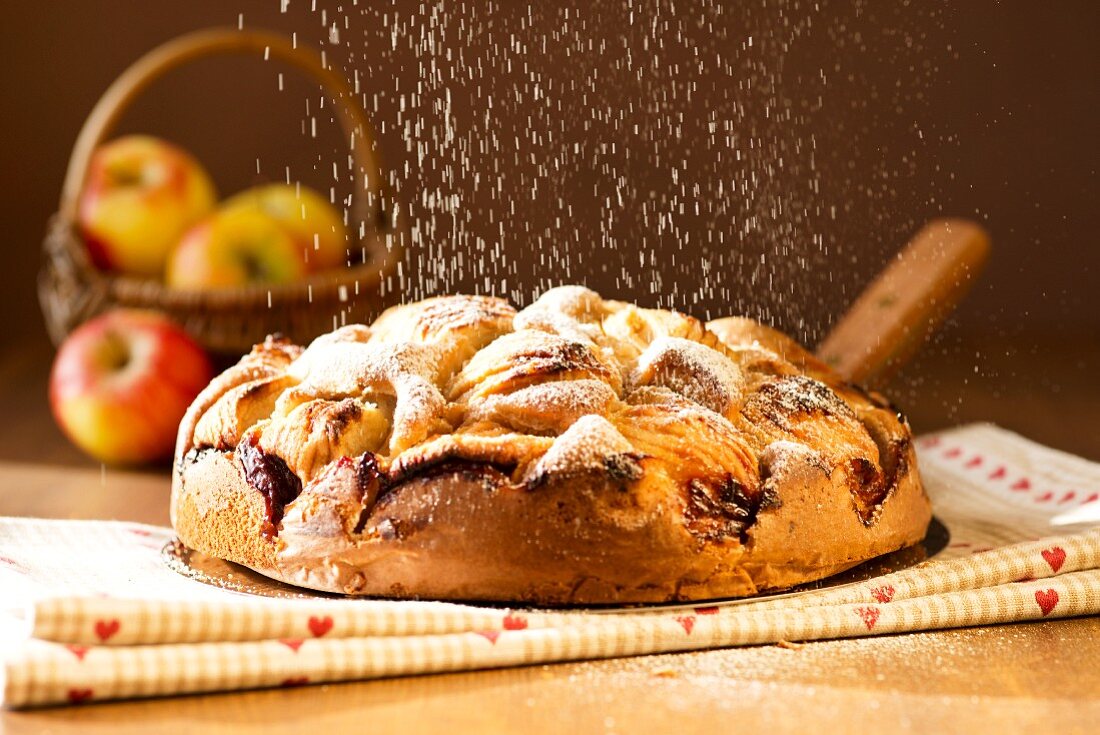 Apple cake being dusted with icing sugar