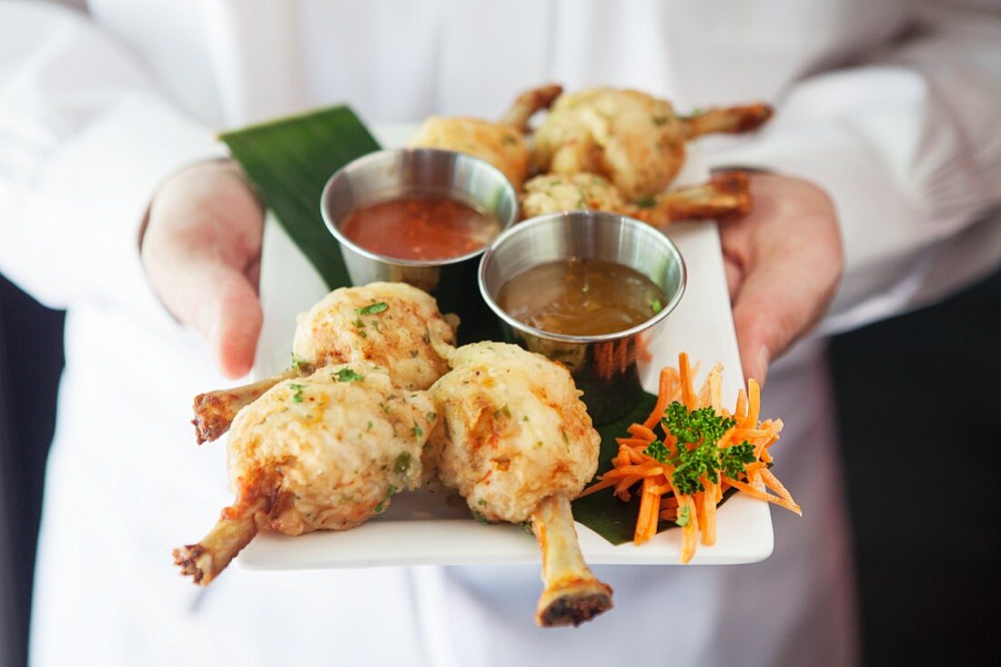 A chef serving pastry coated chicken legs with sauces