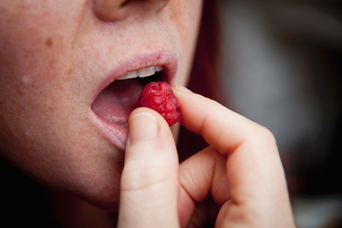 A woman eating a fresh raspberry