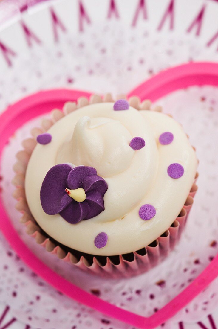 A cupcake decorated with a purple sugar flower on a paper doily