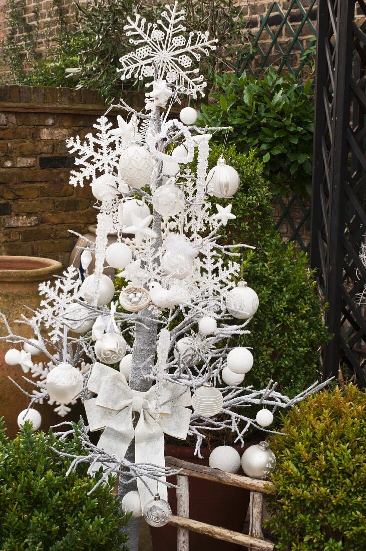 Imitation Christmas tree with white baubles and decorations in wintery garden