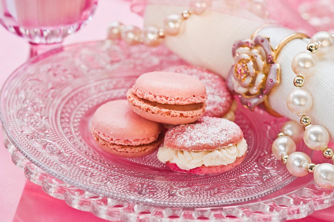 Pink macaroons on a glass plate with a pearl necklace and a napkin