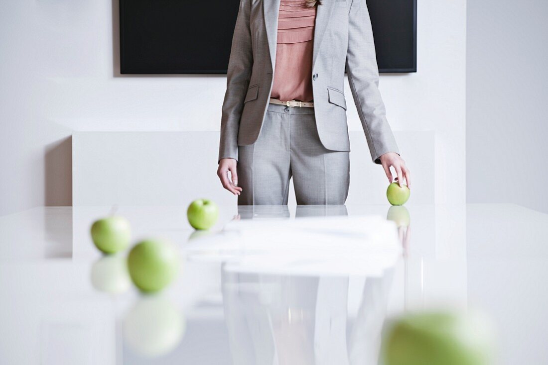 Rollende Äpfel auf Konferenztisch, im Hintergrund Geschäftsfrau