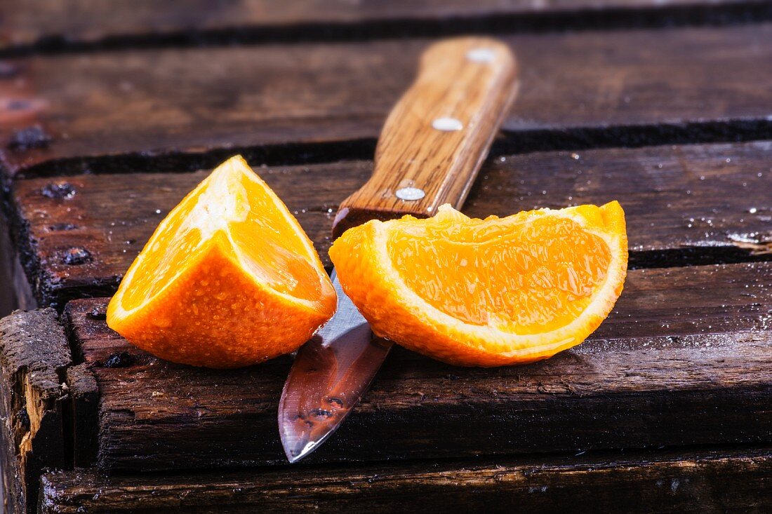 Two orange wedges with a knife on a wooden crate