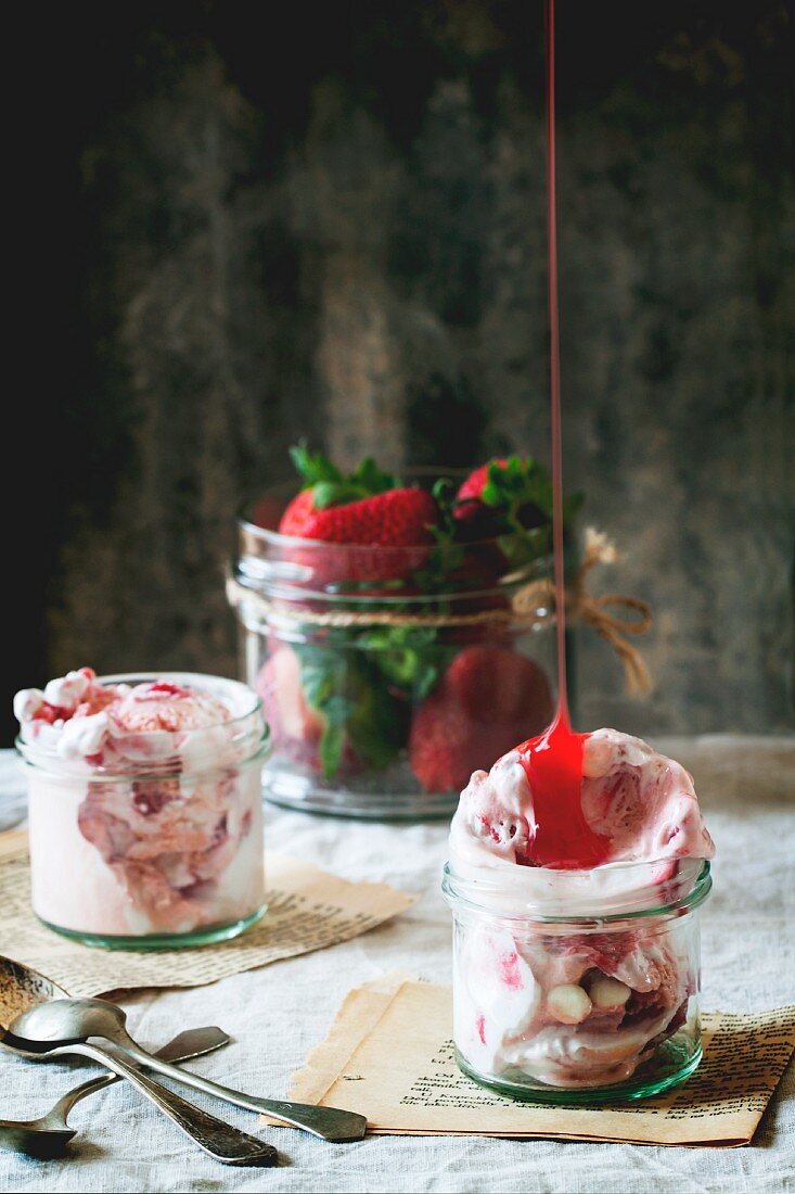 Syrup being poured over strawberry ice cream in a glass jar