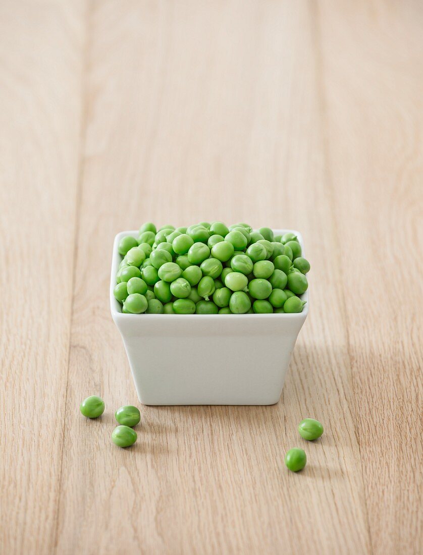 A bowl of fresh peas on a wooden table