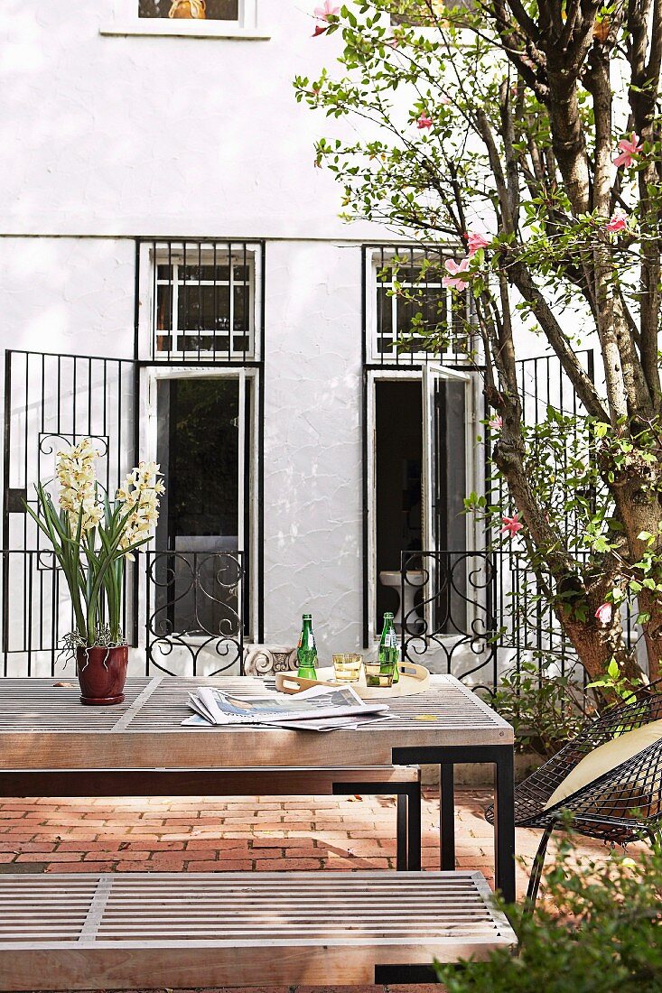 Modern outdoor table and benches in courtyard of house with open metal grilles on terrace doors