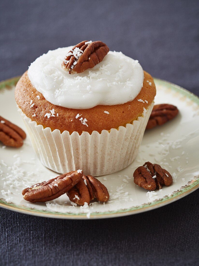 A coconut cupcake decorated with pecan nuts